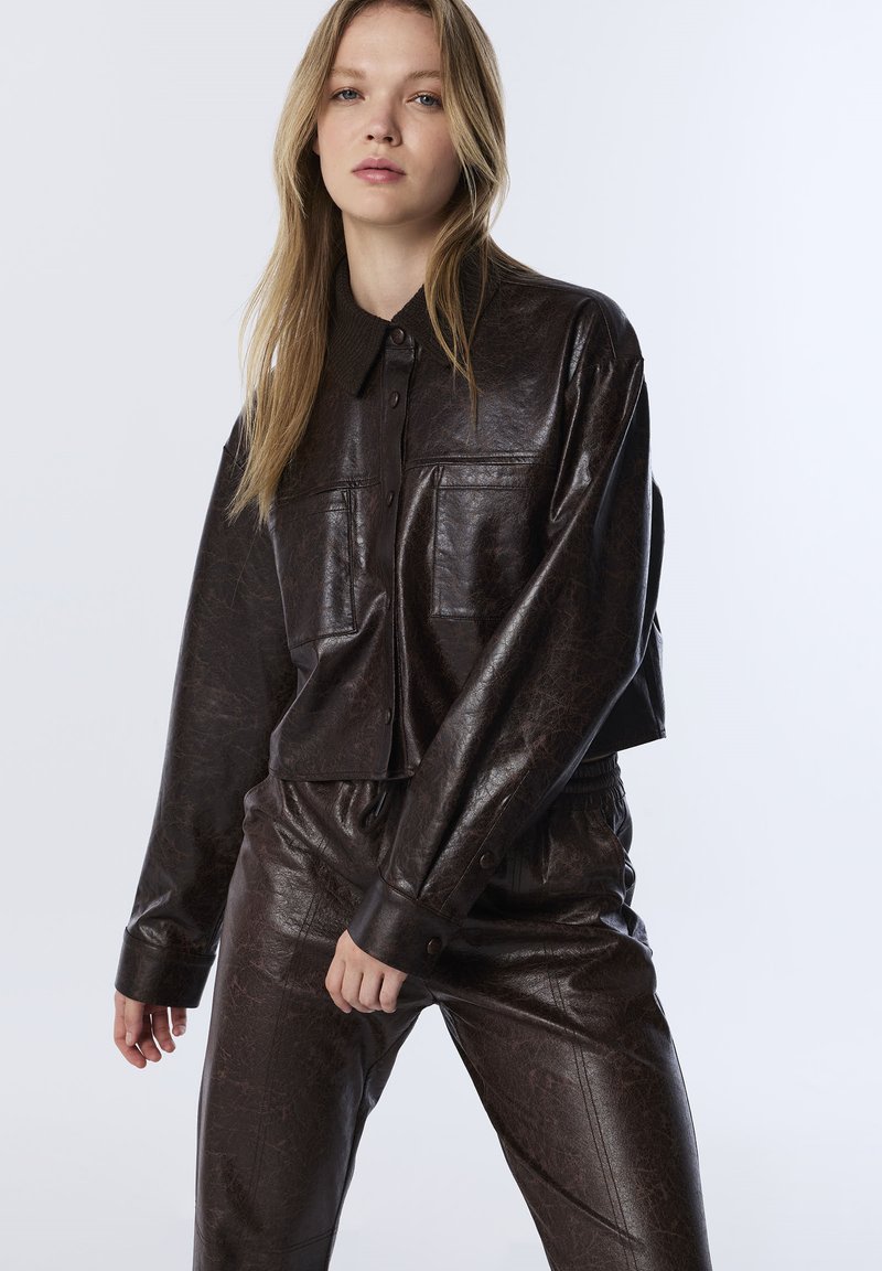 Bruine faux leren jack met een kraag, voorzakken en een cropped ontwerp, gecombineerd met bijpassende faux leren broeken.