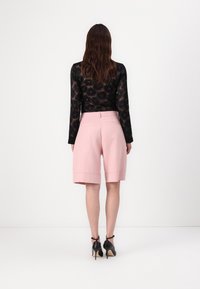 Černý top s dlouhým rukávem a květinovým krajkovým vzorem, spárovaný s bledě růžovými šortkami na míru, které mají boční kapsy a délku těsně nad kolena.