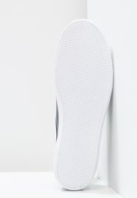 Vit sneaker med en texturerad gummisula med ett zick-zack-mönster, släta grå sidor och en strömlinjeformad design.