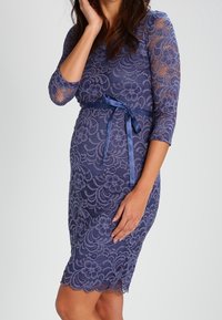 Blå spetsklänning med trekvartsärmar, blommönster, en figursydd midja och ett satinband i midjan. Kantlinjen har en scalloped kant.