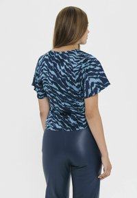 Top blu patterned con maniche corte e scollatura a girocollo, con una vestibilità fluida, abbinato a pantaloni scuri e eleganti.