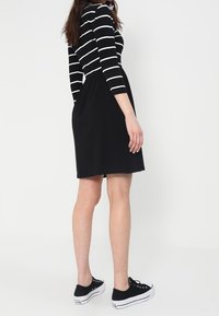 Schwarzes Kleid mit einem gestreiften Oberteil mit langen Ärmeln, figurbetontem Mieder und ausgestelltem Rock, kombiniert mit schwarzen Sneakers. Glatte Stoffstruktur.