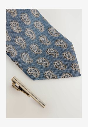 Blue paisley tie with intricate white and gold patterns; textured fabric. Silver tie clip placed beside it, featuring a sleek design.