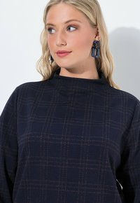 Maglietta a maniche lunghe blu navy con un sottile motivo a scacchi in marrone chiaro e bordeaux. Collo alto e una texture morbida.