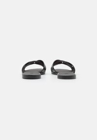 Mustad mustad sandaalid minimalistlikus disainis, millel on sile nahataoline ülemine osa ja lihtne, paindlik põhi. Ilma esmaseid detaile või aksessuaare.