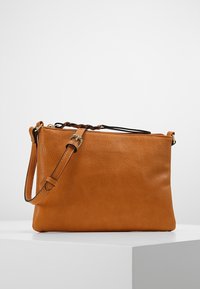 Väri: ruskea, nahkainen crossbody-laukku, jossa on karkea pinta, säädettävä olkahihna ja vetoketjukiinnitys. Yksinkertainen suorakulmainen muoto, jossa on vähäisesti kiinnityksiä.