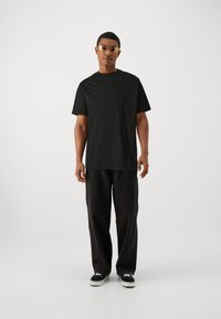Black cotton t-shirt with short sleeves paired with loose black jeans. Model wears yellow sunglasses and black sneakers. Simple design.