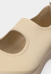 Béžová nazouvací bota s pleteným svrškem, kulatým výřezem na vrchu a měkkou podrážkou, navržená pro pohodlné a každodenní nošení.