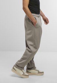 Graue Jogginghosen mit einem elastischen Bund und seitlichen Taschen, kombiniert mit beigen Turnschuhen, die über strukturierte Akzente und ein weiches Material verfügen.