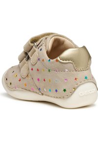 Sneaker beige in suede con accenti metallici dorati, due cinghie in Velcro e motivi a stelle multicolori sul lato esterno. Suola in gomma bianca.