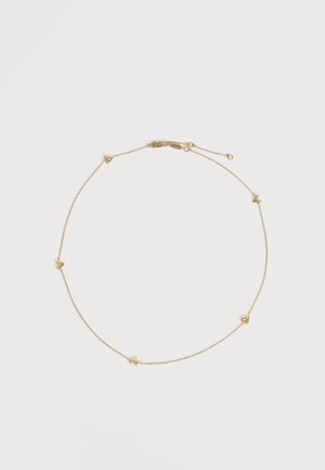 Collier délicat en chaîne dorée, orné de petits pendentifs anguleux et muni d’un fermoir réglable, disposé en cercle sur un fond clair uni.