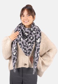 Écharpe à motifs gris et noir en tissu doux, stylée en forme triangulaire, drapée autour du cou sur un pull beige épais.