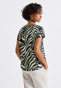 Short-sleeve top featuring a green and cream zebra stripe pattern. Made of a lightweight fabric with a relaxed fit and rounded hem.