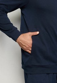 Námořnická modrá mikina s dlouhými rukávy, která má přední kapsu a hladkou texturu, zdobená jemnými švy.