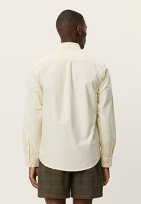 Μακρυμάνικο πουκάμισο σε ανοιχτό κίτρινο χρώμα με στρογγυλεμένο τελείωμα, κουμπωτά μανίκια και κεντρική πλάγια πιέτα στην πλάτη. Κατασκευασμένο από μαλακό, υφασμένο βαμβακερό μείγμα.