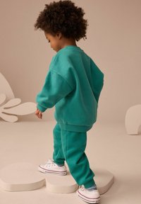 Tealfärgad bomullsset bestående av sweatshirt och sweatpants, med avslappnad passform och ribbade muddar, tillsammans med vita sneakers med röda ränder.