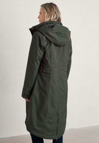 Zelený zateplený kabát s kapucí, strukturovanou podšívkou, bočními knoflíky a dlouhým designem. Obsahuje kapsu na zip blízko lemu.