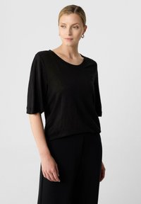 Czarny krótki top z krótkim rękawem wykonany z lekkiego materiału, o luźnym kroju i okrągłym dekolcie. Widoczne detale szwów wzdłuż rękawów i ciała.