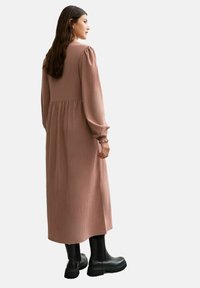 Robe longue à côtes de couleur rose doux, avec des manches bouffantes et une taille froncée. Associée à des bottines noires brillantes.