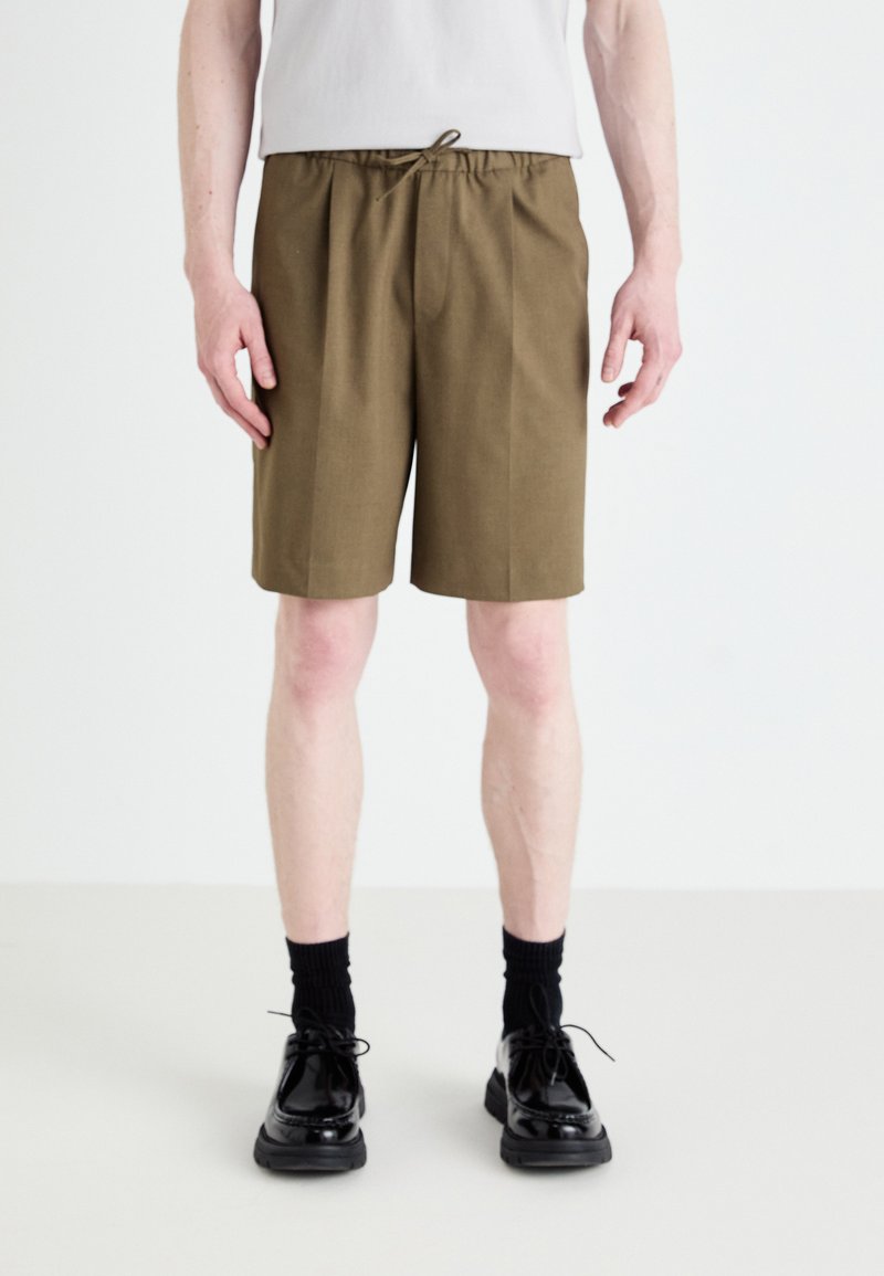 Khaki shorts met een elastische tailleband en een trekkoord, voorzien van een rechte pijp en een gestructureerde afwerking, gecombineerd met glanzende zwarte schoenen.