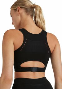 Czarny sportowy biustonosz z wycięciem na plecach typu racerback, detalem wycięcia oraz różowym przeszyciem. Wykonany z teksturowanej tkaniny z regulowanymi elementami.