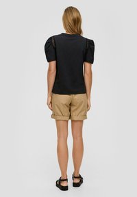 Zwarte t-shirt met pofmouwen en kantdetails op de schouders, gecombineerd met kaki shorts met omslagen. Plat sandalen gedragen.