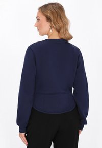 Sudadera corta azul marino con mangas largas, puños acanalados y cuello redondo. Textura suave y detalles de costura en la cintura.