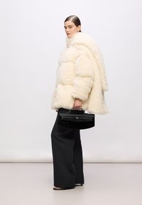 Cream fur puffer jacket with a high collar, paired with wide black trousers and a textured black handbag featuring a handle.