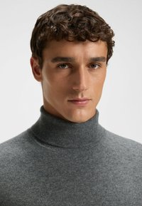 Szary sweter na golfie wykonany z miękkiego, cienkiego materiału, z wysokim kołnierzem i długimi rękawami, wyeksponowany na neutralnym tle.