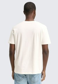 Korte mouwen, licht crèmekleurig t-shirt van zacht materiaal met een ronde hals. Losse pasvorm, gladde textuur en geen zichtbare grafische elementen of patronen.