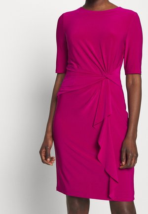 Robe ajustée magenta longueur genou avec manches au niveau des coudes, encolure bateau, et détail de nœud froncé avec volant en cascade sur le côté droit devant.