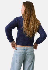 Granatowy sweter dzianinowy z prążkowanymi mankietami i dołem, w połączeniu z jasnoniebieskimi spodniami o wysokim stanie. Sweter ma teksturowane wykończenie.