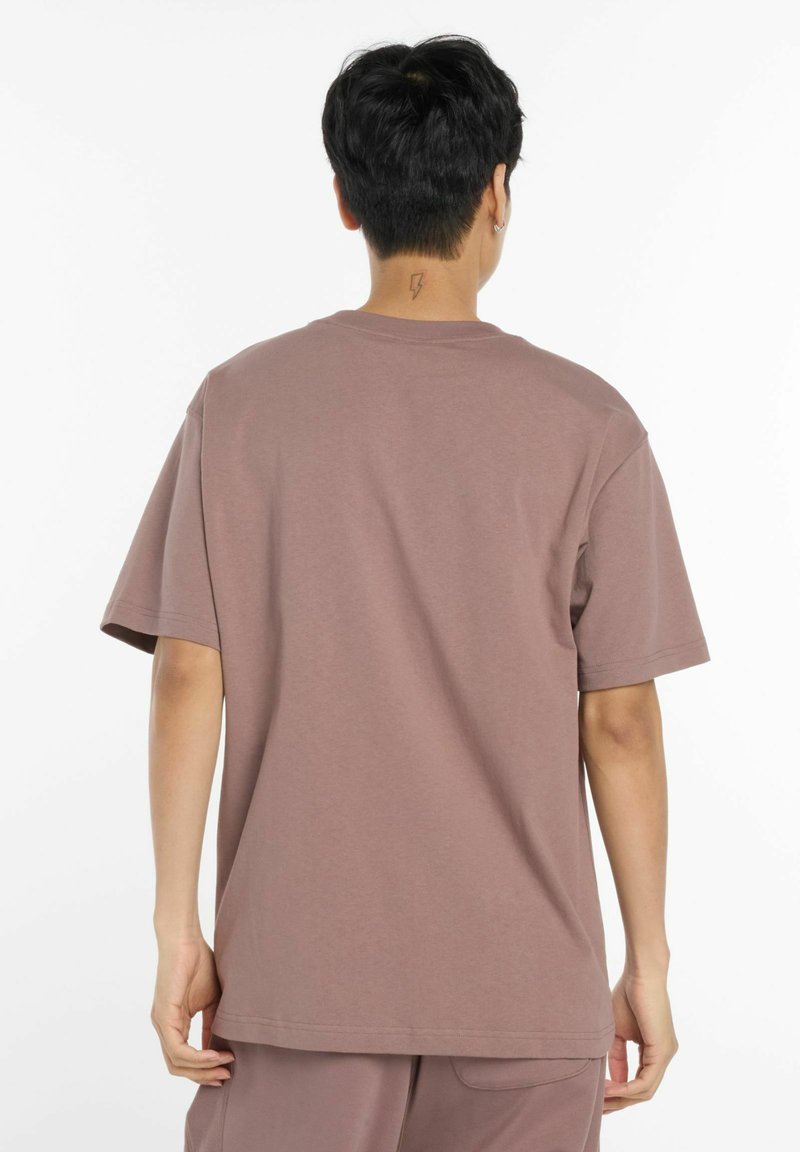 Lyhythihainen, rento T-paita hillityssä mauven sävyssä, valmistettu pehmeästä kankaasta, jonka pyöreä pääntie ei sisällä erottuvia kuvioita tai koristeita.