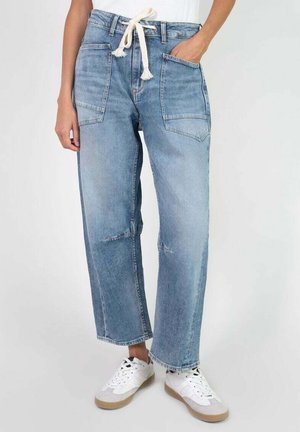 Light blue denim wide-leg jeans with a drawstring waist, multiple pockets, and a faded finish. Worn with white sneakers.
