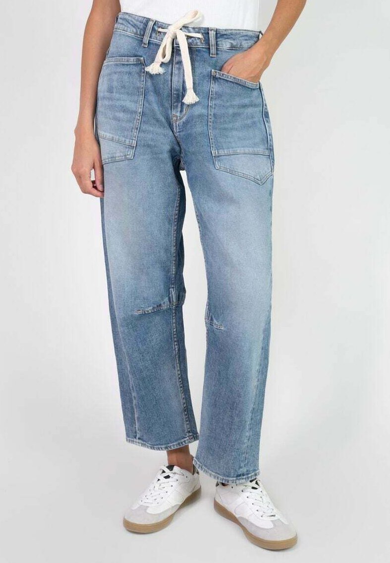 Jeans en denim bleu clair à jambes larges avec une taille à cordon, plusieurs poches et une finition délavée. Portés avec des baskets blanches.