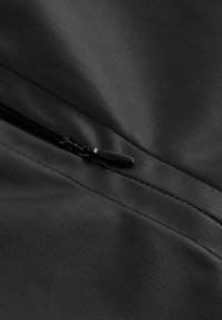 Indumento in ecopelle nera con cuciture in vista e una tasca con zip. La zip è in metallo nero con un elegante tirante.