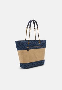 Sac fourre-tout en tissu matelassé bleu marine avec une base en osier tressé, équipé de poignées doubles, de quincaillerie dorée et d'une poche zippée sur un côté.