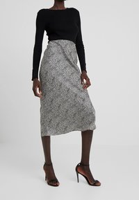 Haut noir à manches longues assorti à une jupe blanche mi-longue à motifs noirs en taches, complété par des sandales à talons hauts et à brides.