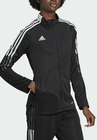 Černá sportovní bunda Adidas se zipovým uzávěrem, bílými třemi proužky na ramenou a rukávech a hladkým, lehkým materiálem.