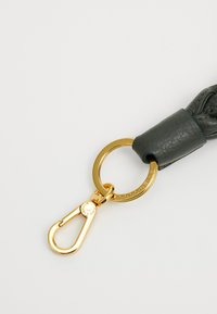 Leder-Schlüsselanhänger in Dunkelgrün, mit geflochtenem Design und einem goldfarbenen Metallverschluss. Auffälliger runder Ring mit eingeprägtem Markennamen.