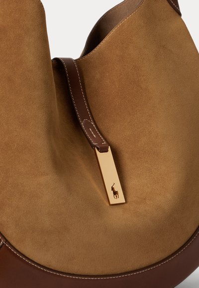 Sac à main en daim beige et cuir marron avec une étiquette rectangulaire dorée arborant un petit logo cheval et cavalier sur le devant.