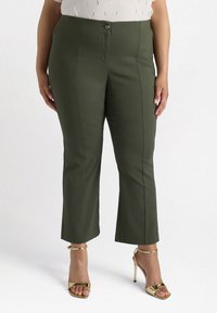 Olivově zelené kalhoty s přiléhavým střihem, předním zipem a knoflíkovým zapínáním, zúženými nohavicemi a bočními kapsami. Nosené s zlatými sandály na vysokém podpatku.