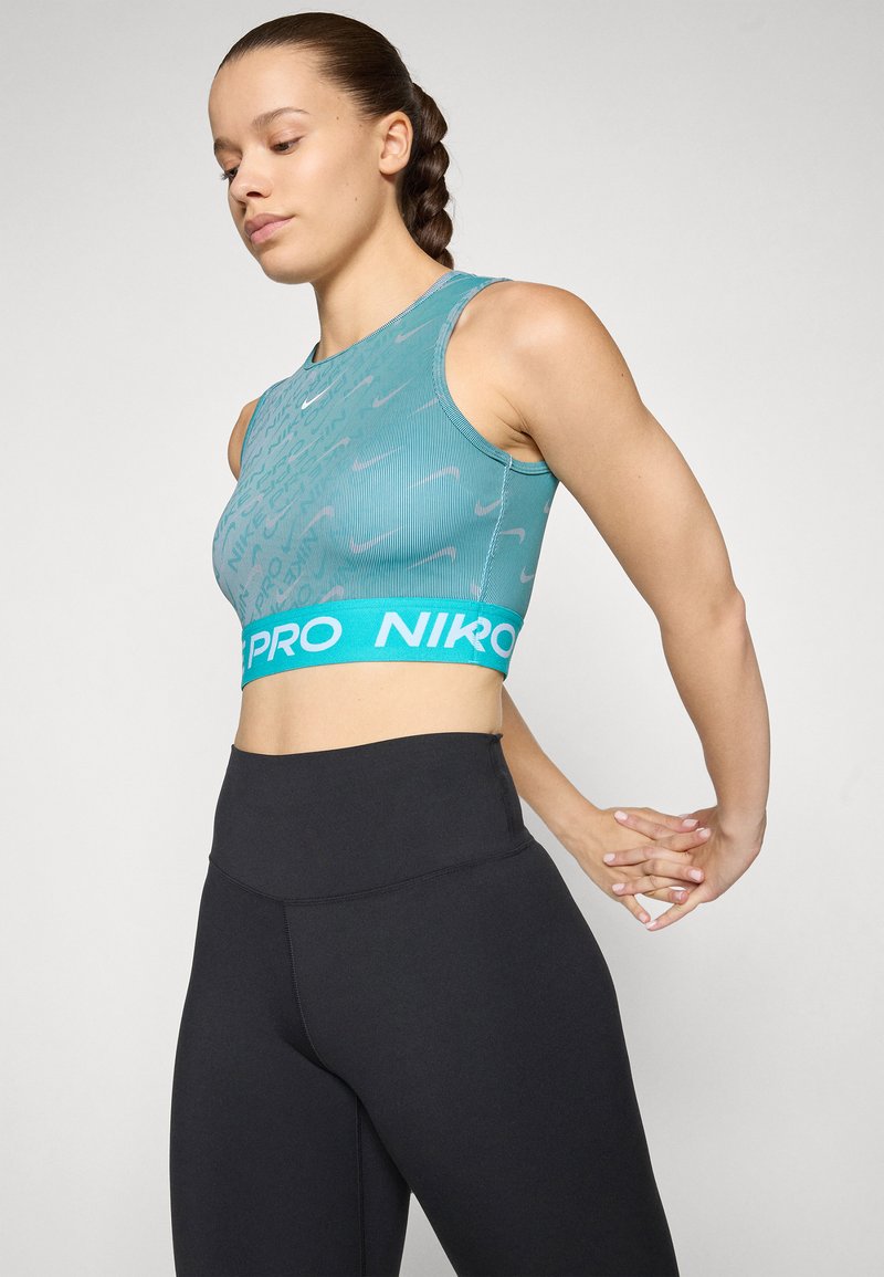 Cropped top sportivo di un azzurro chiaro con un motivo testurizzato e una ampia banda turchese con la scritta "NIKE PRO". Indossato con leggings neri a vita alta.