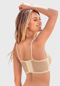 Beige kanten bh met doorzichtig achterpaneel, verstelbare bandjes, intrigerende kantdetails op de cups en haaksluiting. Soepele textuur en figuurvormend ontwerp.