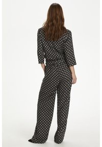 Combinaison noire à motifs avec des manches trois-quarts, coupe ample et taille cintrée. Présente des motifs circulaires dans des couleurs atténuées.