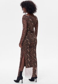 Sukienka z długim rękawem w brązowo-beżowy wzór węża, z bocznym rozcięciem, marszczeniem w talii i dopasowanym krojem. Czarne botki na obcasie.