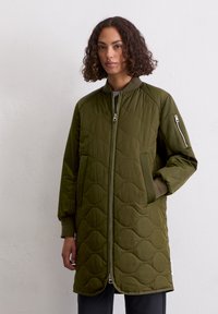 Groene gewatteerde lange jas met een staande kraag, ritsluiting en zijzakken; heeft een gestructureerd patroon en ribbels aan de mouwen.