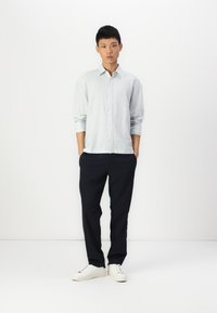 Camisa azul claro e branca em riscas, com um corte descontraído, combinada com calças escuras azul-marinho e sapatilhas brancas. Design simples, aparência casual.