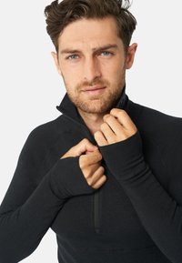 Schwarz zip-up Pullover mit langen Ärmeln und Daumenlöchern. Hat einen hohen Kragen und einen weichen, strukturierten Stoff. Figurbetonter Schnitt.