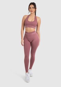 Completo activewear di un delicato colore mauve, composto da un top corto a collare e leggings a vita alta, realizzati in tessuto morbido e elasticizzato con dettagli del logo.
